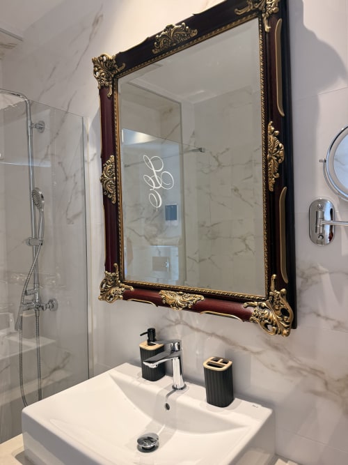 Lujoso cuarto de baño en Edificio San Esteban Sevilla con espejo de marco dorado ornamentado, paredes de mármol y modernas griferías.