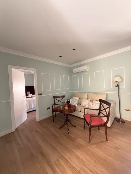Salón elegantemente amueblado en la Suite Julio César del hotel Sevilla con sofá crema, mobiliario de madera y paredes verde pálido
