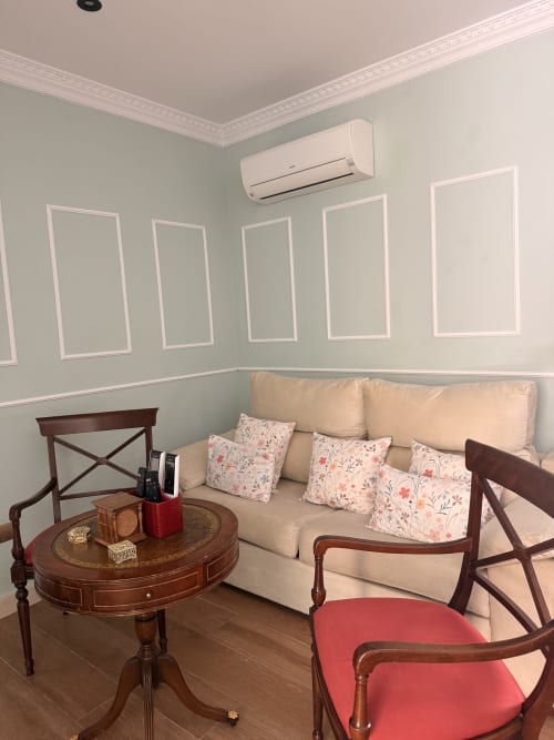 Elegante sala de estar en el Edificio San Esteban de Sevilla con sofá crema, cojines florales, muebles de madera y aire acondicionado split