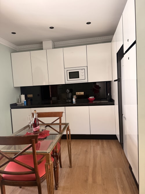 Moderna cocina-comedor en apartamento de Sevilla con muebles blancos, encimera negra, mesa de madera y sillas rojas