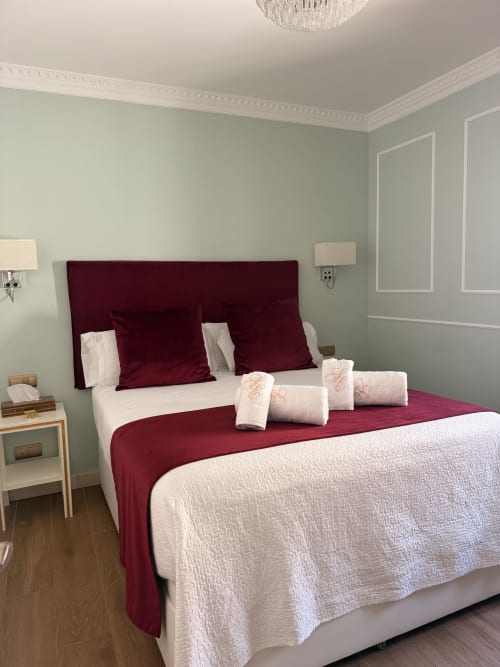 Dormitorio de lujo en Edificio San Esteban 16 de Sevilla con cabecero de terciopelo burdeos, ropa de cama crema y toallas dobladas