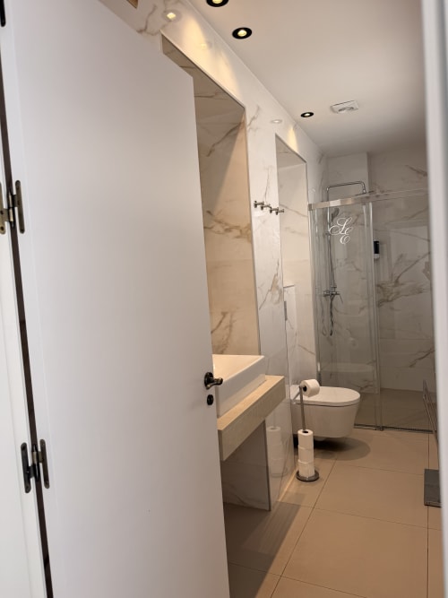 Baño moderno en la suite Edificio San Esteban 16 Sevilla con paredes de mármol, ducha de cristal, inodoro y espejo de tocador