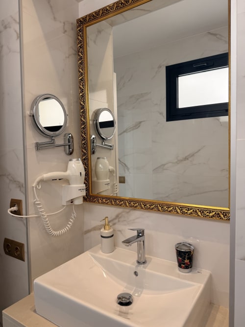 Baño de mármol en suite del Edificio San Esteban 16 Sevilla con espejo de marco dorado ornamental, dos lavabos y servicios modernos