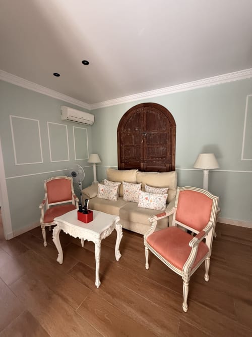 Elegante sala de estar en la Suite Mañara, Edificio San Esteban, Sevilla, con sofá beige, butacas coral y puerta arqueada de madera
