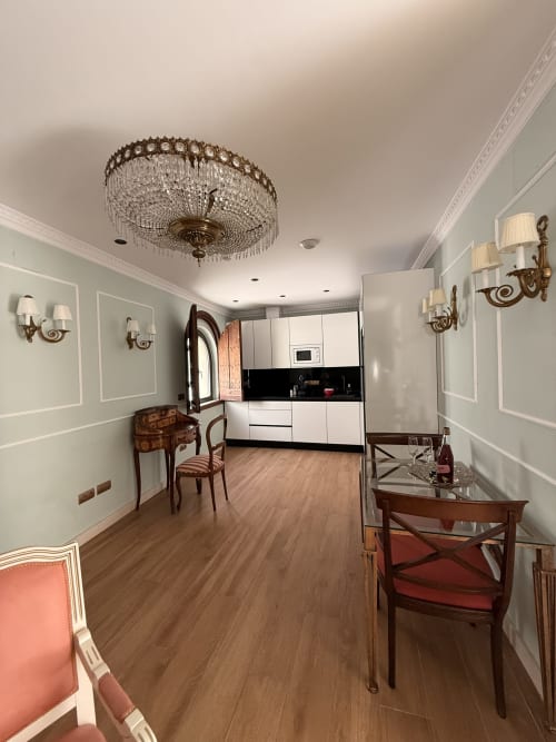 Elegante cocina y comedor de apartamento en Sevilla con muebles blancos, lámpara de cristal, suelos de madera y detalles antiguos