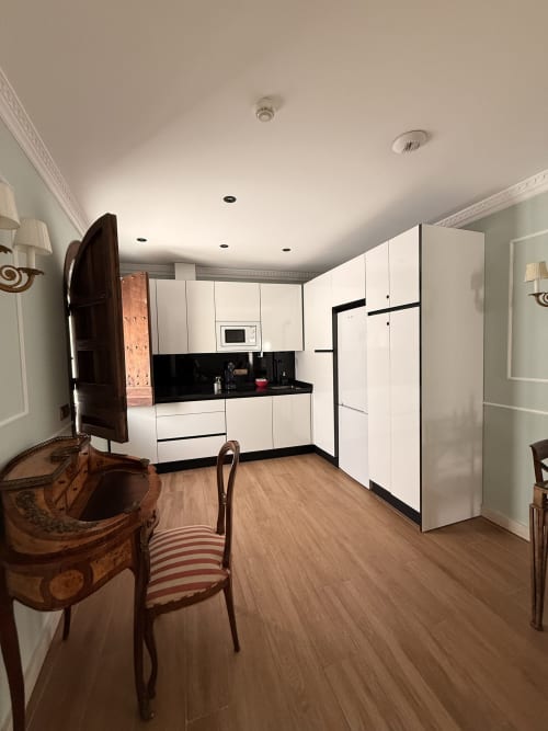 Cocina moderna con armarios blancos y encimeras negras en suite de hotel en Sevilla, con zona de comedor y pisos de madera