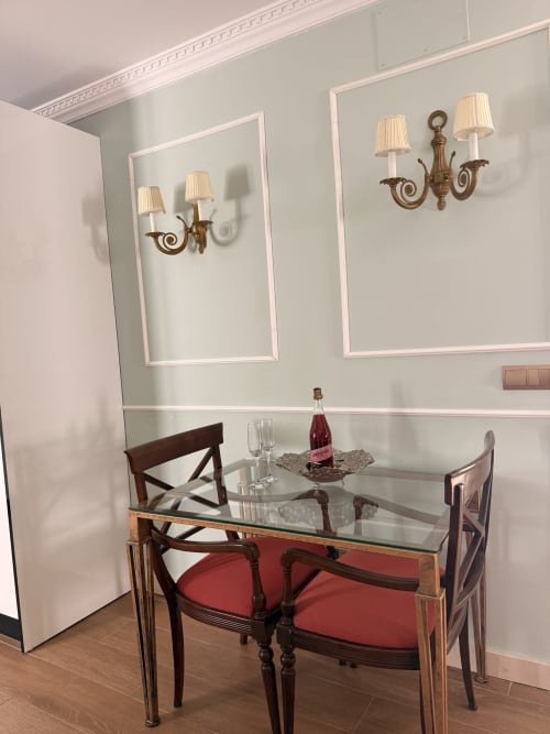 Elegante comedor en suite de hotel sevillano con mesa de cristal, sillas tapizadas en rojo y apliques de bronce