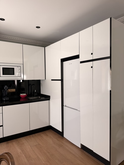 Cocina moderna en suite de hotel sevillano con muebles blancos, encimeras negras, electrodomésticos de acero inoxidable y suelo de madera