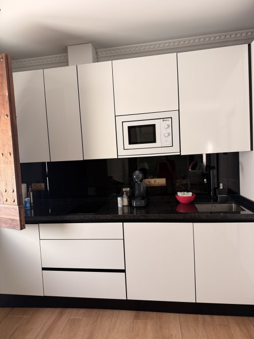 Cocina moderna blanca con encimera negra y microondas en la Suite Mañara del Edificio San Esteban, Sevilla