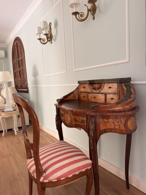 Elegante escritorio con silla de rayas rojas en suite de hotel en Sevilla, con detalles de madera marquetería y apliques de latón