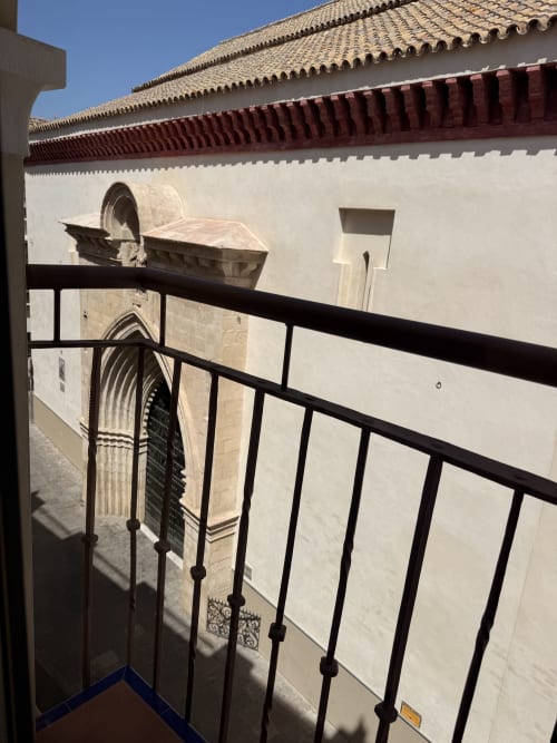Barandilla de balcón con herrería negra vista hacia un edificio histórico blanco con portada de arcos en San Esteban, Sevilla