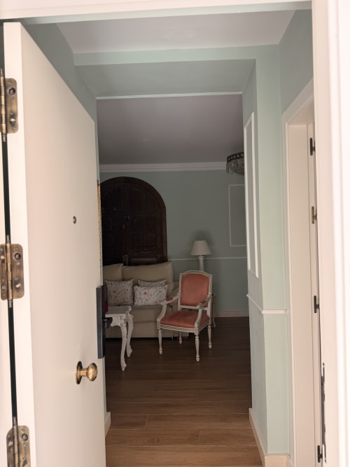 Elegante pasillo de dormitorio en Edificio San Esteban 16, Sevilla, con paredes azul pálido, suelos de madera y mobiliario de época