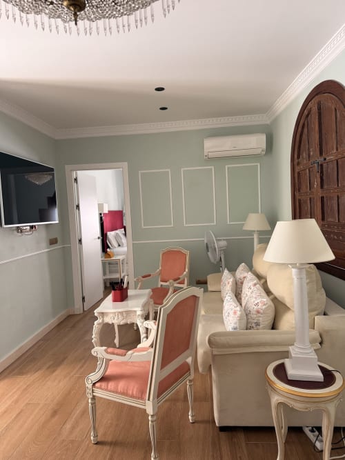 Elegante sala de estar de la Suite Mañara en Sevilla con sofá crema, sillas coral, araña ornamental y muebles de época