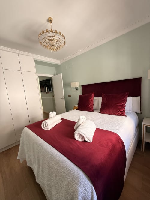 Elegante suite de dormitorio en Edificio San Esteban 16, Sevilla, con acentos burdeos y lámpara de cristal