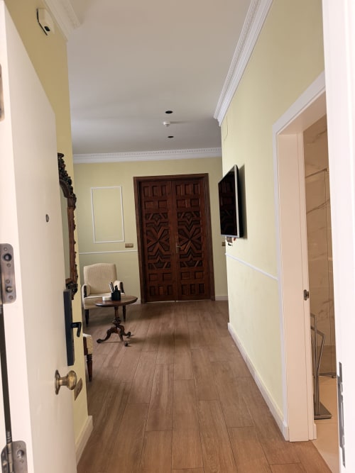 Elegante pasillo en apartamento sevillano con paredes amarillas, suelos de madera, puertas ornamentadas y moderno televisor