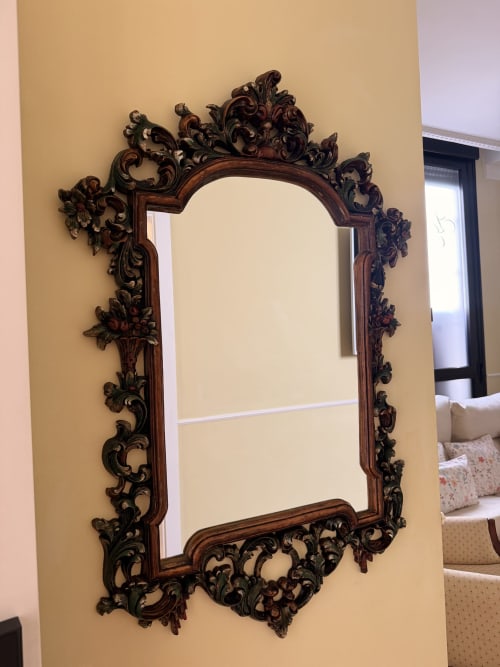 Espejo tallado en madera oscura con ornamentación barroca en pared beige de suite de hotel en Sevilla