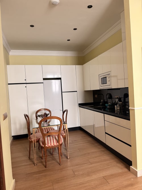 Cocina y comedor modernos en apartamento de Sevilla con muebles blancos, encimeras negras y mobiliario de madera