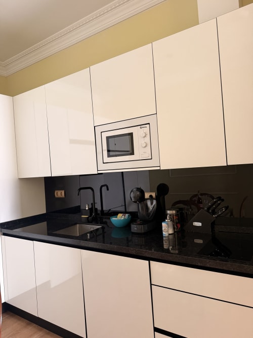Cocina moderna en apartamento de Sevilla con muebles blancos, encimera negra y microondas integrado