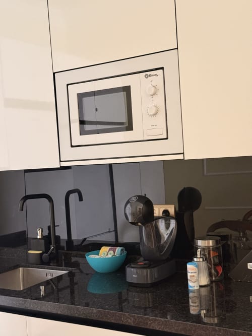 Cocina moderna con microondas Baley empotrado, encimera negra y electrodomésticos de acero inoxidable en suite del hotel de Sevilla