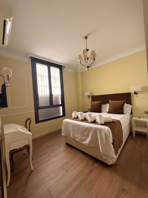 Elegante dormitorio en Edificio San Esteban 16 de Sevilla con paredes amarillas, cama de madera oscura, araña de cristal y detalles de madera