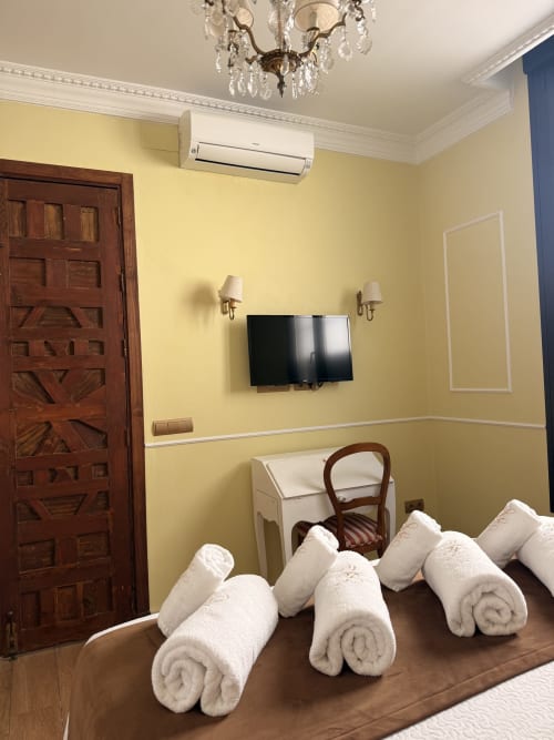 Dormitorio amarillo en Edificio San Esteban 16, Sevilla, con toallas enrolladas en cama, TV mural y equipamiento moderno
