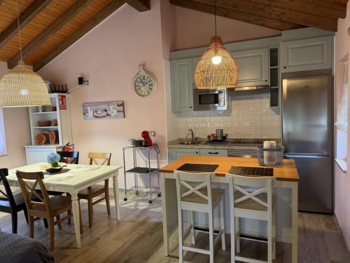 Cocina comedor abierta en la casa rural C'Genoveva, Biescas Asturias, con vigas de madera, lámparas colgantes tejidas y