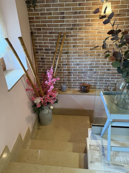 Escalera de propiedad rural asturiana con paredes de ladrillo, flores decorativas rosa en jarra y muebles tradicionales
