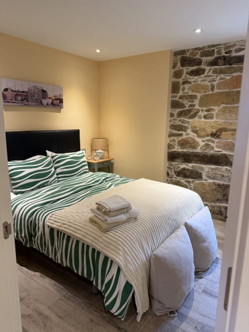 Dormitorio acogedor con ropa de cama de rayas verdes, cabecero negro, pared de piedra y paredes amarillo cálido en casa rural asturiana