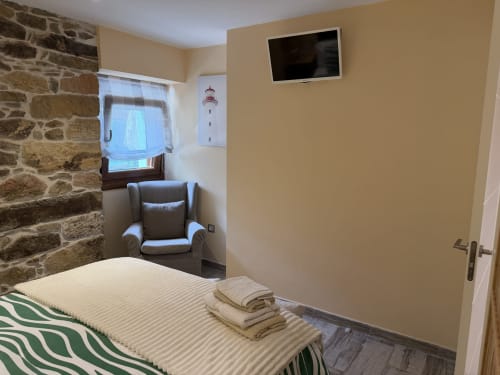 Acogedor dormitorio en el hotel rural CaleaCabo de Asturias con muros de piedra, sillón, TV de pantalla plana y vistas a la montaña