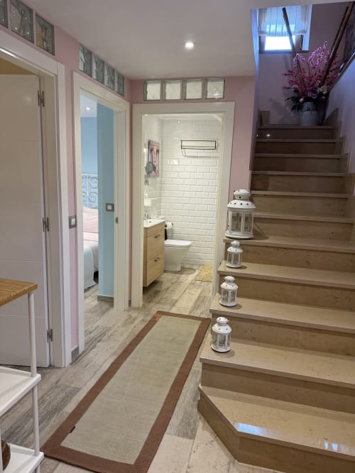 Pasillo rústico con escaleras de madera, paredes rosa, baño blanco y faroles decorativos en hotel rural asturiano