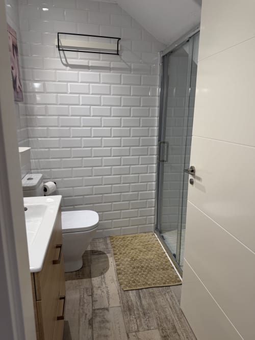 Baño moderno del hotel rural CaleaCabo, Asturias con azulejos tipo metro blancos, inodoro, lavamanos, ducha y detalles de madera