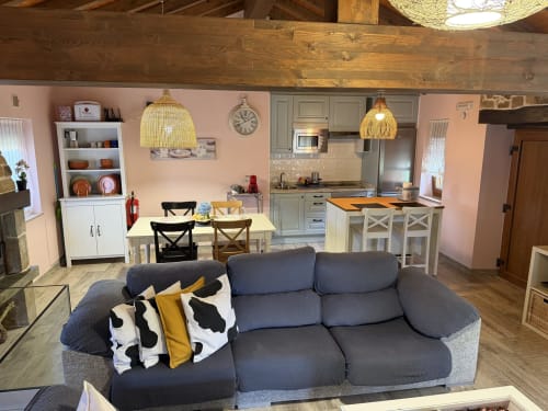 Sala de estar diáfana con sofá gris, mesa de comedor, cocina y chimenea en casa rural asturiana