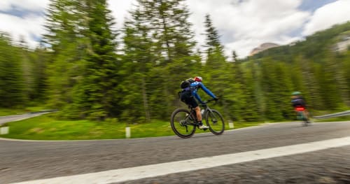 Ciclista in maglia blu che pedala su strada di montagna vicino a Ceva, Italia, con colline boscose e sfondo montano