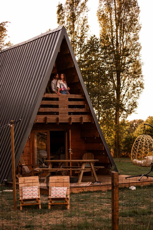 Couple sur le balcon d'un chalet A-frame à Mesnil & Une Nuit, entouré de bouleaux d'automne et d'un salon de jardin