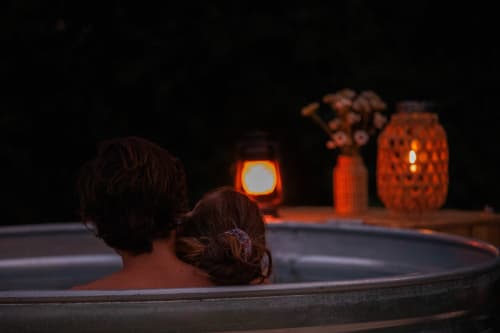 Deux hôtes se détendent dans un bain nordique nocturne, illuminé par des lanternes du jardin du gîte Mesnil & Une Nuit