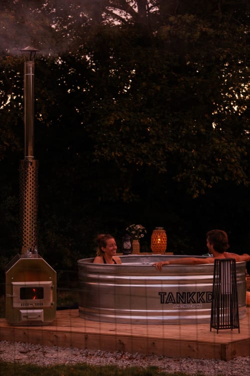 Deux hôtes savourent un bain nordique au gîte Mesnil & Une Nuit, avec poêle chauffé au bois et ambiance de jardin à Gisay la