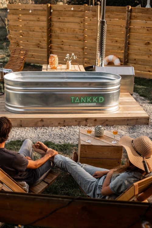 Couple se détendant près du bain nordique du gîte Mesnil & Une Nuit, clôture en bois et verres sur la table
