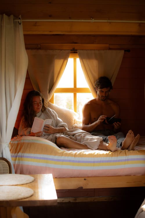 Couple se détendant dans un lit douillet niché en bois à la maison d'hôtes Mesnil & Une Nuit, avec vue sur le jardin et lumière naturelle