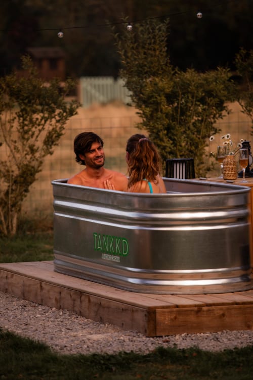 Couple se relaxant dans un bain nordique de la maison d'hôtes Mesnil & Une Nuit, entouré de verdure et de jardin.