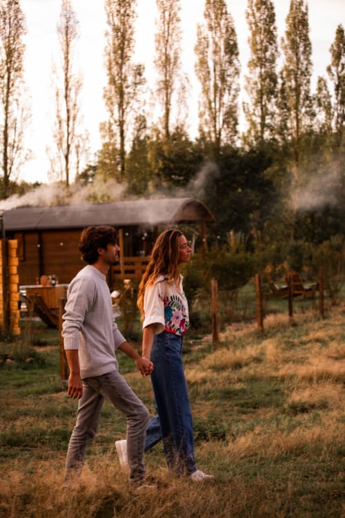 Couple se tenant la main marchant dans le jardin du gîte Mesnil & Une Nuit avec collines et grands arbres