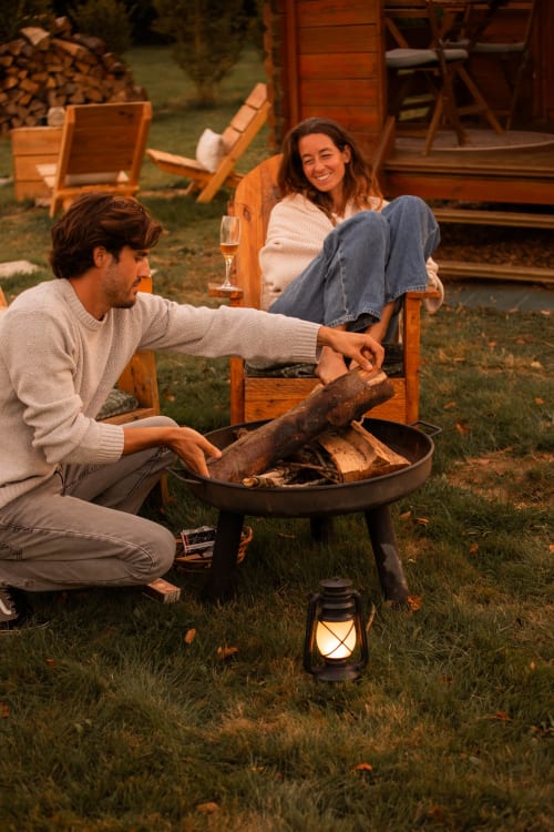 Couple savourant la soirée au coin du feu du gîte Mesnil & Une Nuit en France, avec du vin et des chaises en bois à proximité
