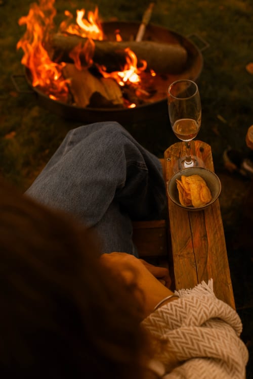Personne dégustant du vin et des amuse-bouches devant un feu de cheminée crépitant au gîte Mesnil & Une Nuit en France
