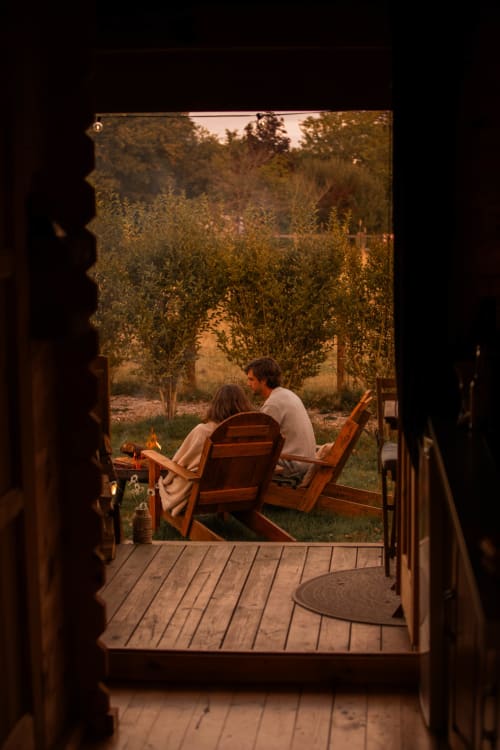 Couple détente dans des fauteuils Adirondack sur la terrasse en bois du gîte Mesnil & Une Nuit, vue sur le jardin