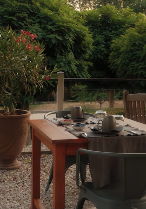 Terrasse de restauration en plein air au Moulin Renaudiots à Autun avec table dressée, fleurs rouges et verdure luxuriante