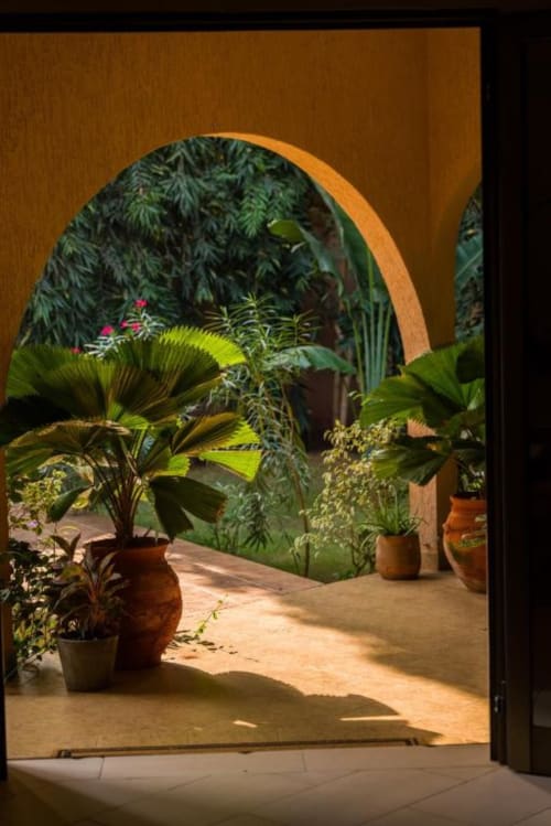 Porche en terre cuite voûté ouvrant sur un jardin intérieur luxuriant aux Nomads Kodjoviakopé à Lomé, Togo