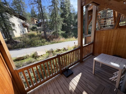 Terrasse en bois avec balustrade de l'appartement Varsea à Vars, vue sur le sentier forestier et les bâtiments environnants