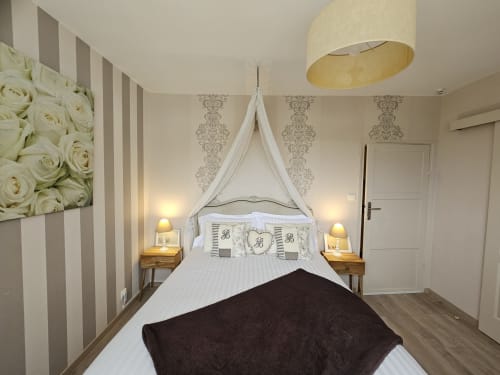 Chambre élégante aux Portes du Hable avec lit à baldaquin, papier peint rayé et œuvres florales.