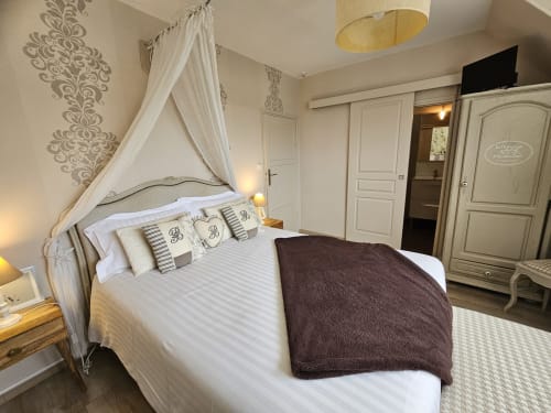 Élégante chambre aux Portes du Hable à Cayeux-sur-Mer : lit à baldaquin, papier peint damassé et mobilier crème