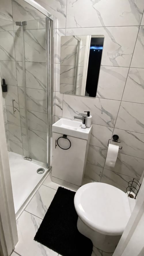 Modern bathroom at La Rose Serenity Residence in London featuring marble tiles, shower enclosure, compact sink, toilet, and