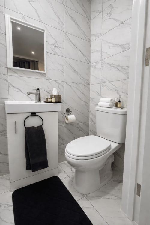Modern marble bathroom at La Rose Serenity Residence in London featuring white sink, toilet, and mirrored cabinet